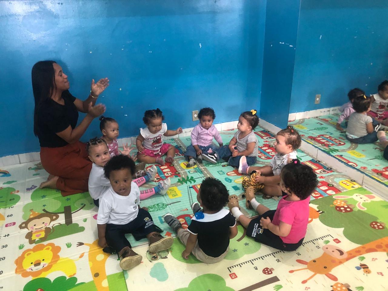 Educadora sentada no chão cantando e interagindo com um grupo de bebês do berçário da Creche Patati-Patatá